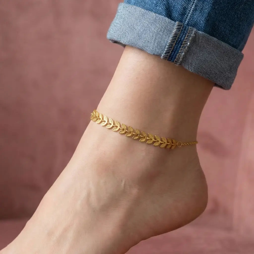Gold anklet on a person's ankle with a blurred pink background
