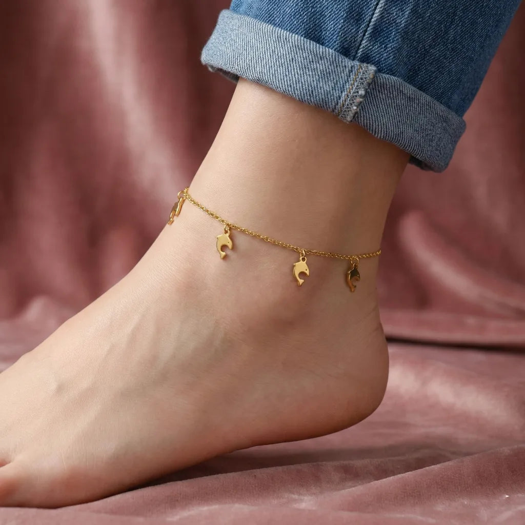 Gold anklet on a foot with a pink background