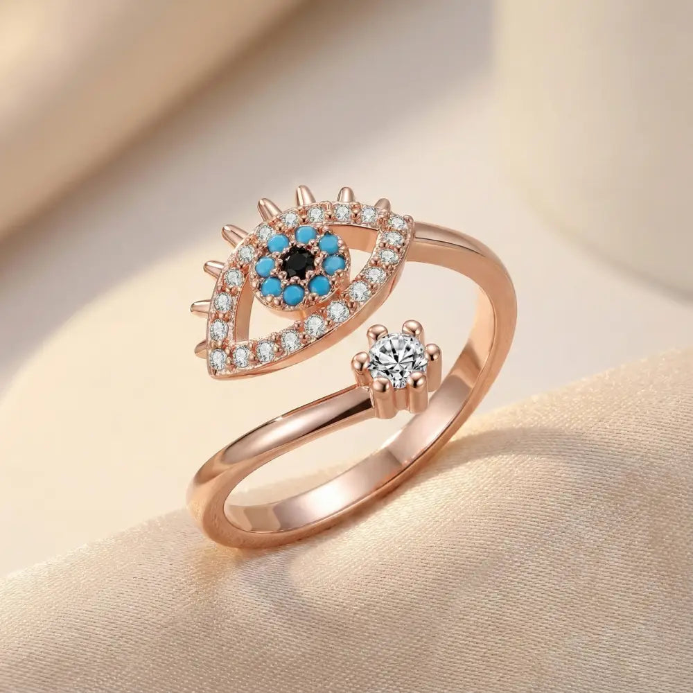 Rose gold ring with eye design and gemstones on a beige background