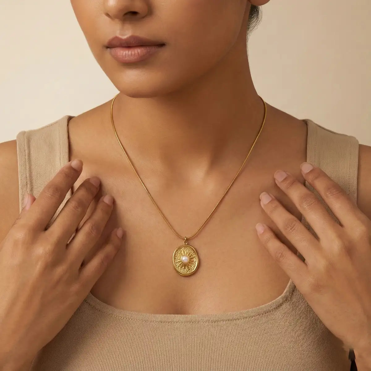 Woman wearing a gold necklace with a pearl pendant against a beige background