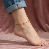Gold anklet on a foot with a blurred pink background