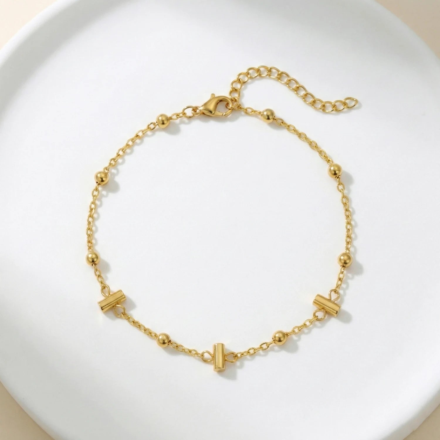 Gold bracelet with geometric beads on a white plate