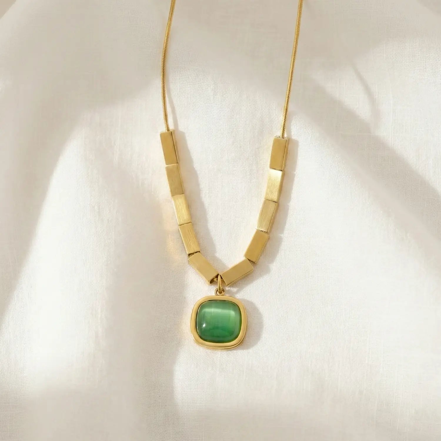 Gold necklace with a green pendant on a white background