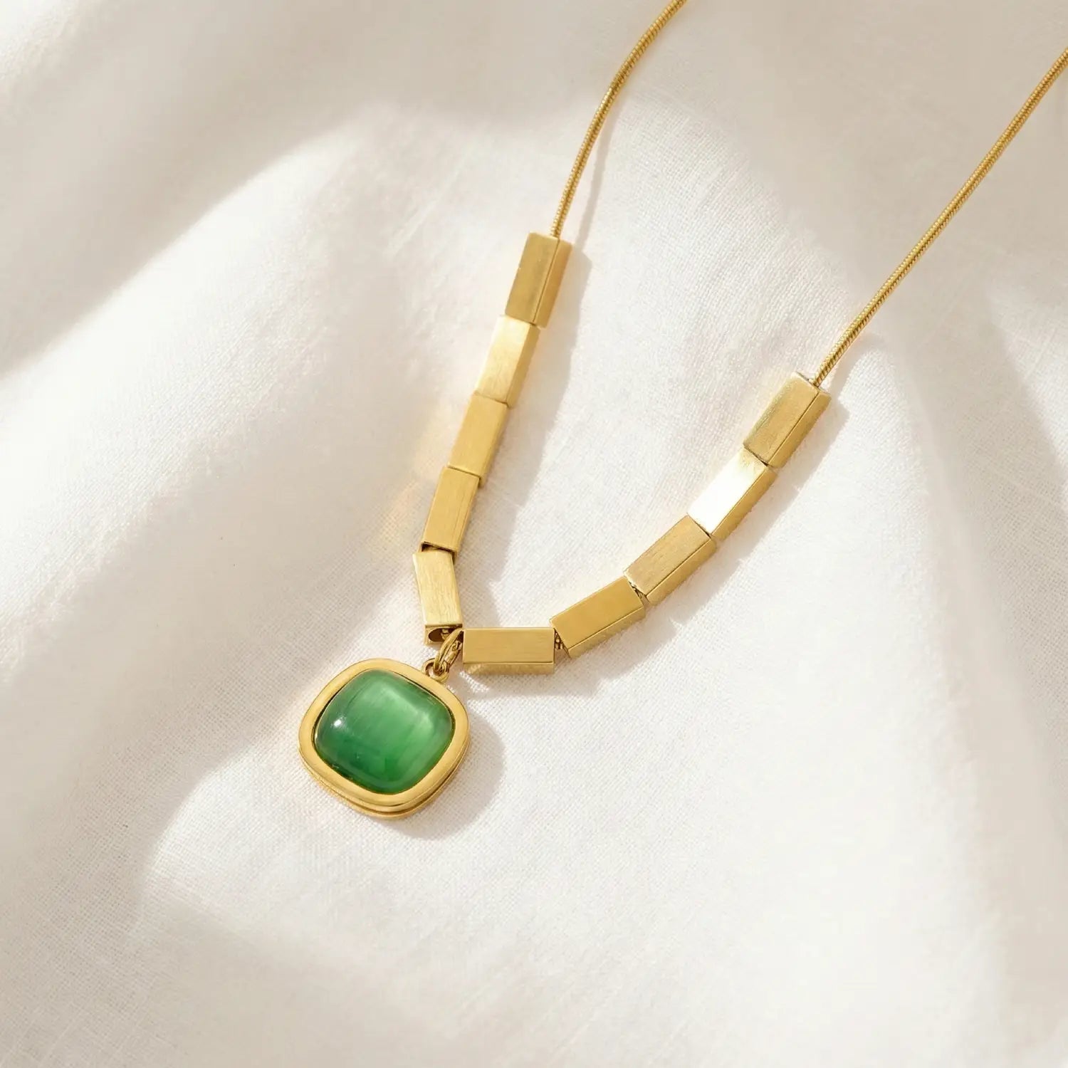 Gold necklace with a green pendant on a white fabric background