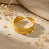 Gold leaf bracelet on a textured beige fabric background with dried flowers.