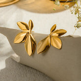 Gold leaf-shaped earrings on a beige stone surface with a soft background