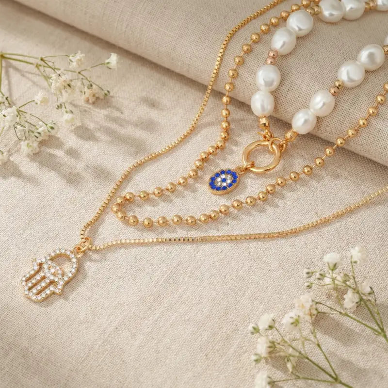 Gold necklace with a blue evil eye pendant and pearl necklace on a beige fabric background with small white flowers.