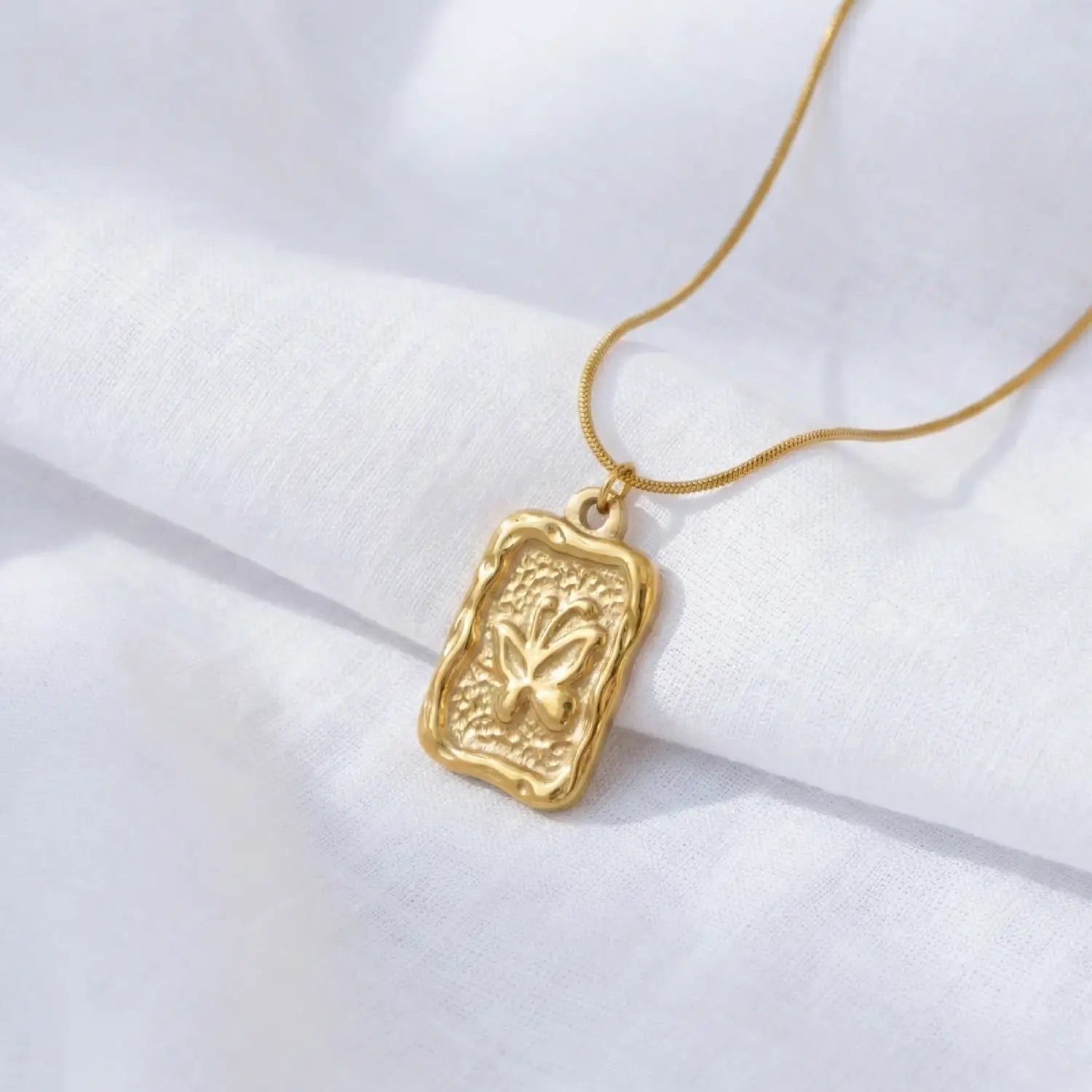 Gold necklace with a rectangular pendant on a white fabric background