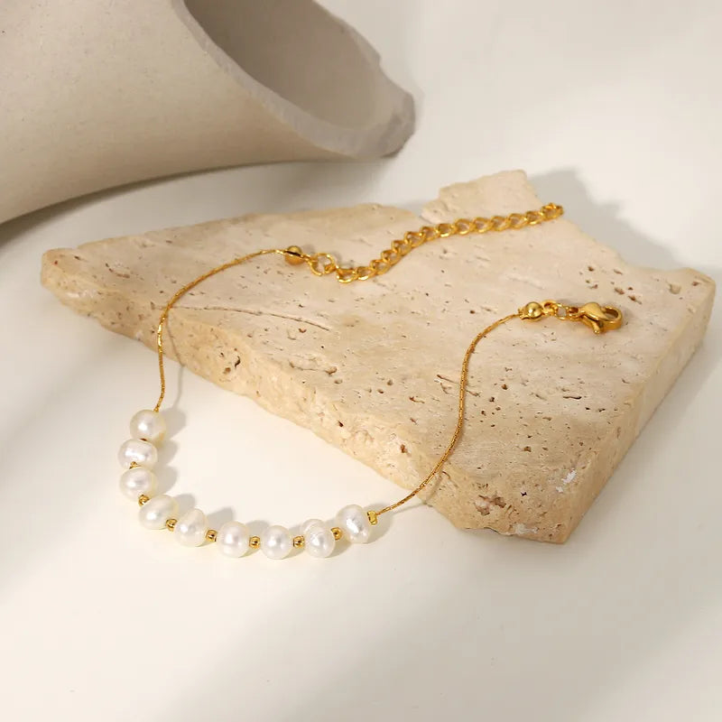 Gold and pearl bracelet on a stone surface with a neutral background