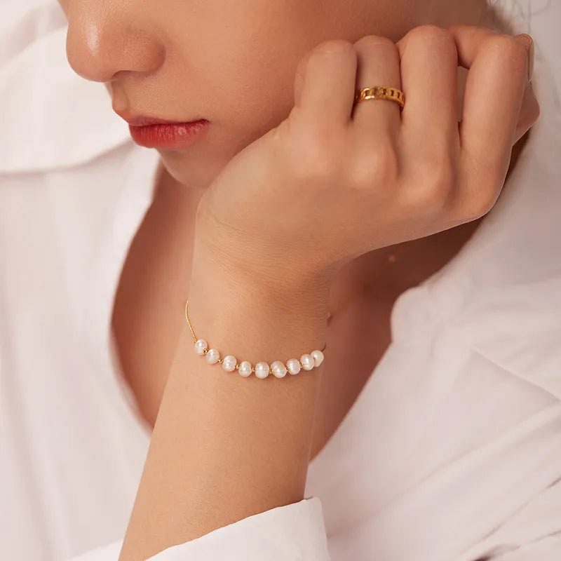 Close-up of a woman's hand wearing a gold ring and pearl bracelet against a white background