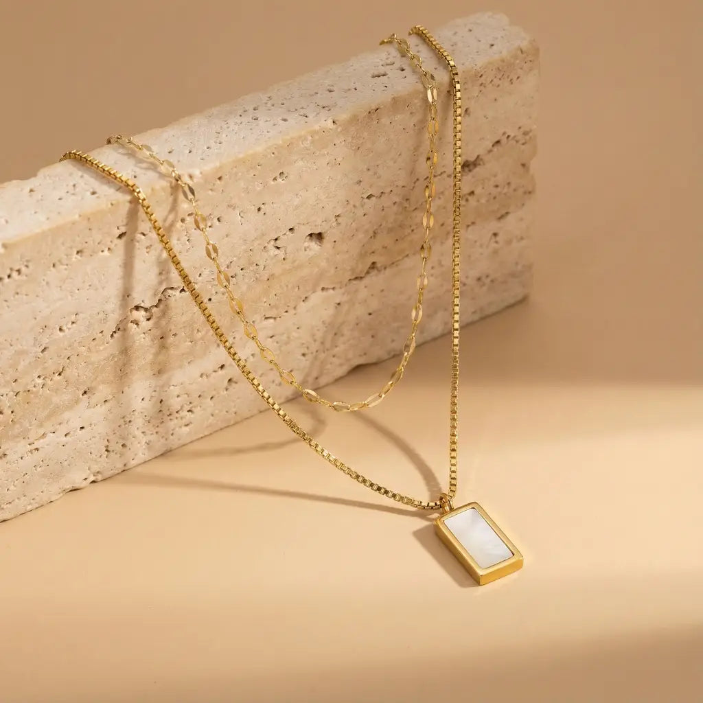 Gold necklace with a rectangular pendant on a beige stone block