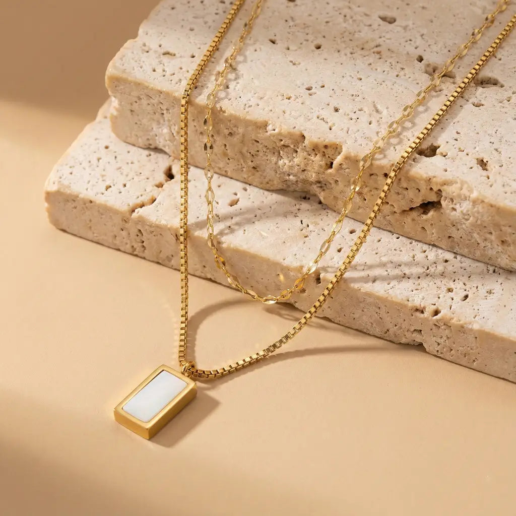 Gold necklace with a rectangular pendant on a textured beige surface