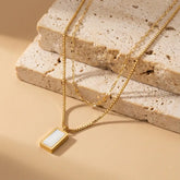 Gold necklace with a rectangular pendant on a textured beige surface