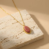 Gold necklace with a pink pendant on a textured stone surface