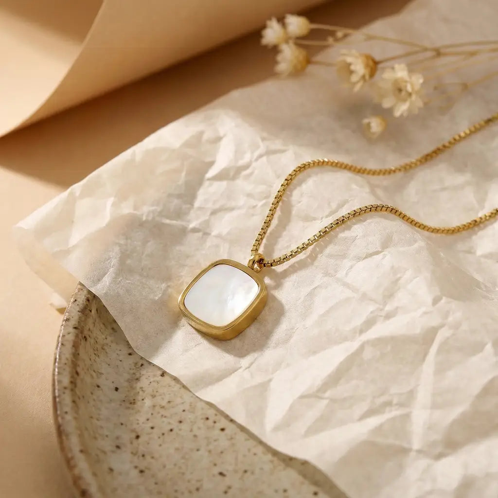 Gold necklace with a square pendant on crumpled paper with dried flowers.