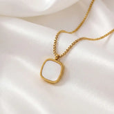 Gold necklace with a white pendant on a white fabric background