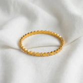 Gold bracelet with hexagonal pattern and small stones on a white fabric background
