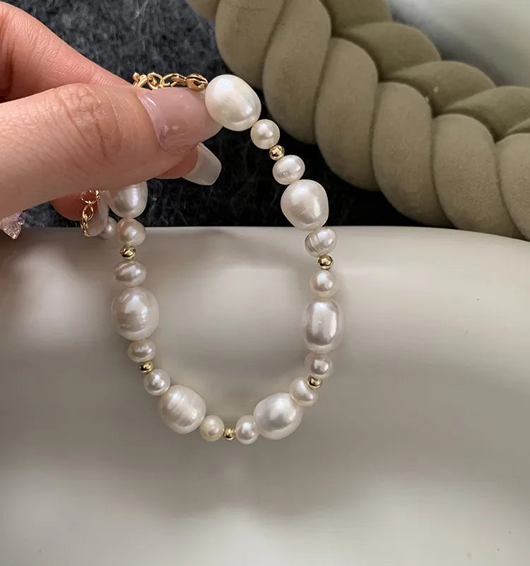 Pearl bracelet with gold accents held by a hand on a neutral background