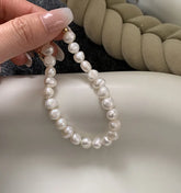 Pearl bracelet held by a hand on a neutral background