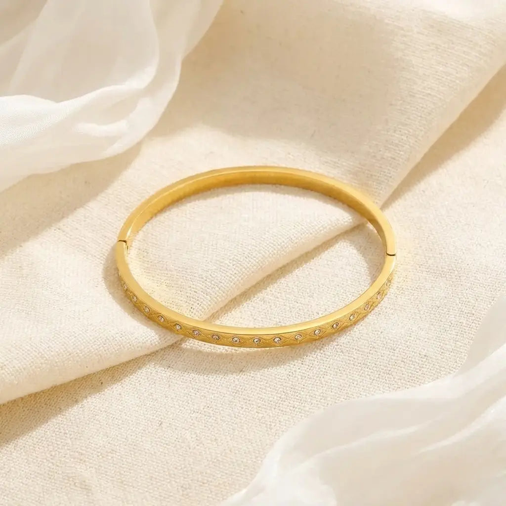 Gold bangle with embedded stones on a soft beige fabric background
