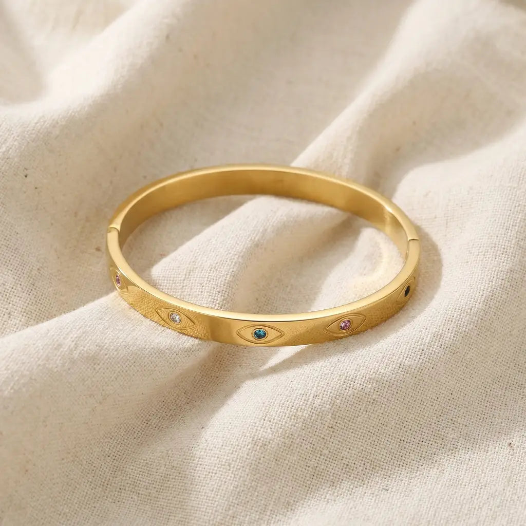 Gold bracelet with embedded gemstones on a beige fabric background