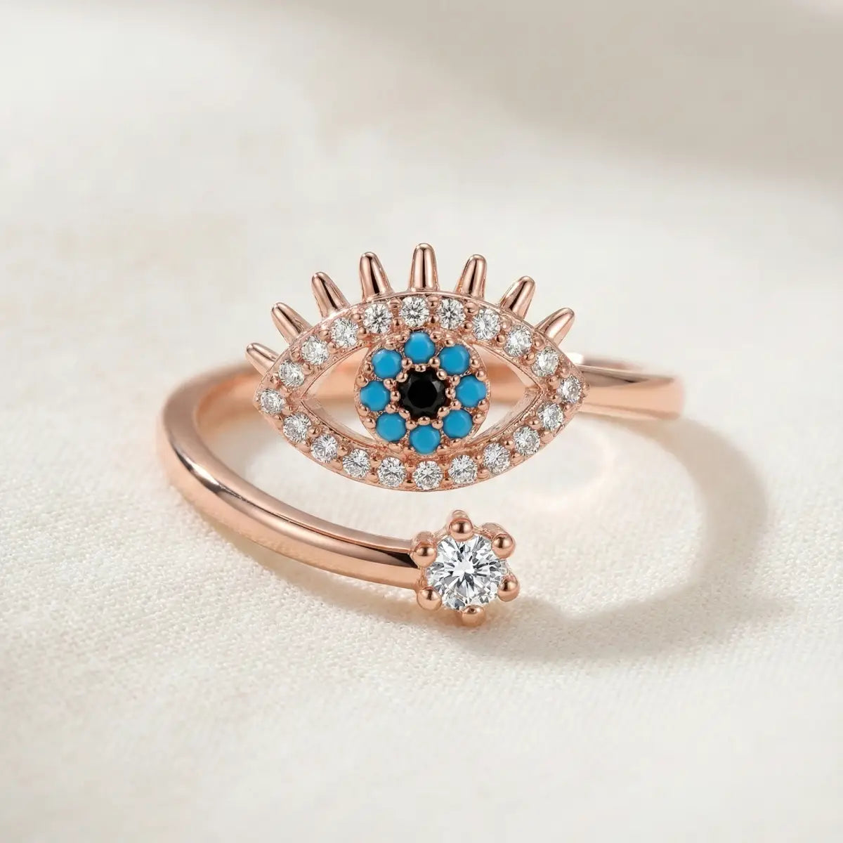 Rose gold ring with eye design and gemstones on a light background