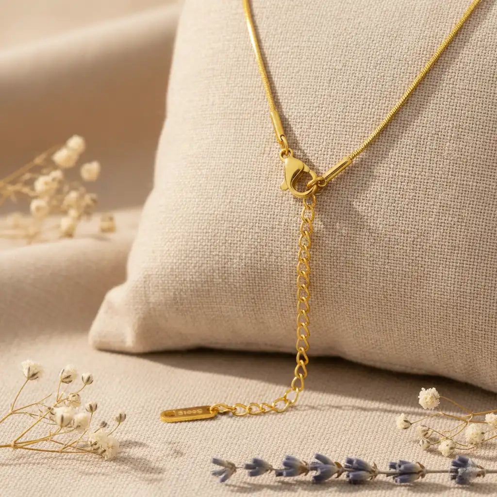 Gold necklace on a textured beige surface with dried flowers