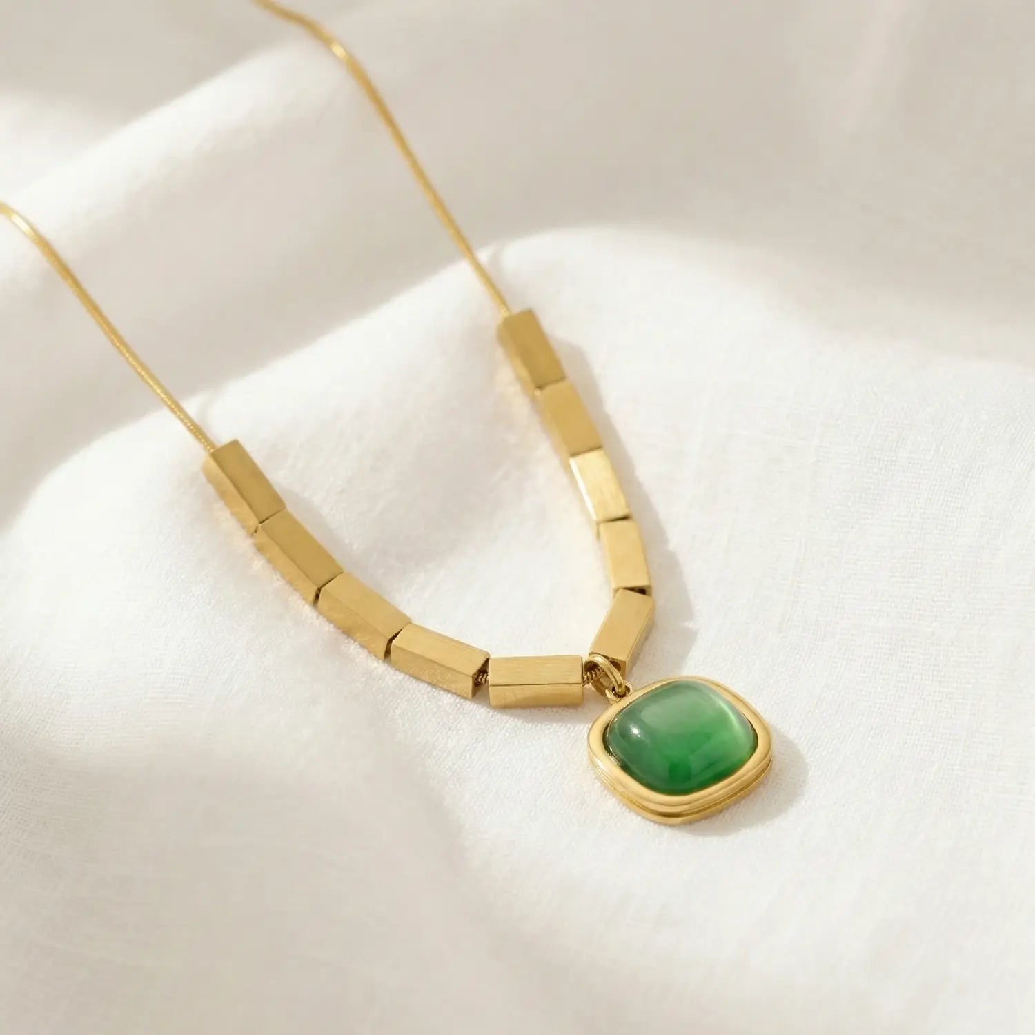 Gold necklace with a green pendant on a white background