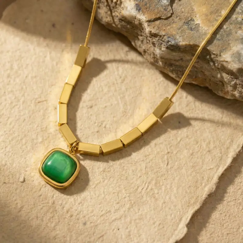 Gold necklace with a green pendant on a stone surface