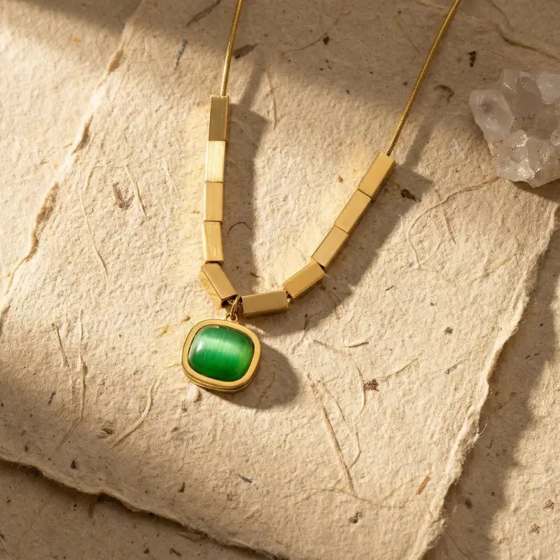 Gold necklace with a green pendant on a textured beige surface