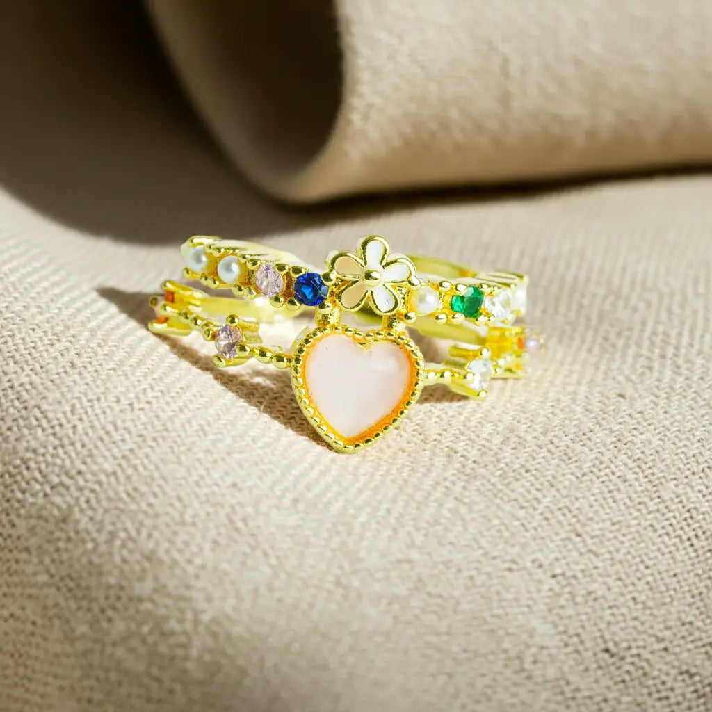 Gold ring with heart and flower design on a beige fabric background