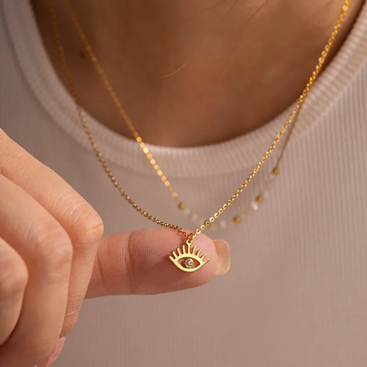 Gold necklace with an eye-shaped pendant held by a hand against a neutral background 800