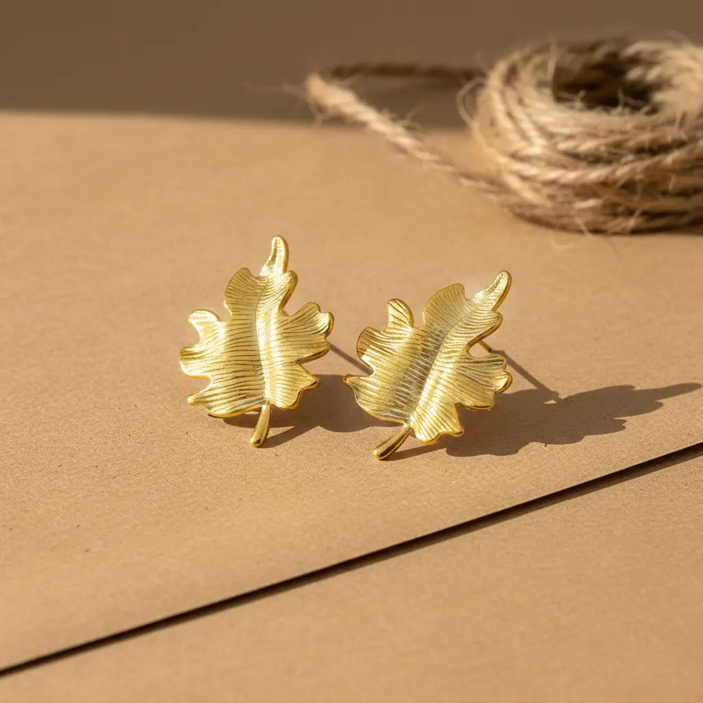Gold leaf-shaped earrings on a beige surface with a rustic background
