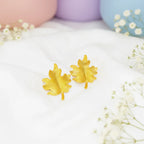 Gold leaf earrings on a white surface with pastel balloons and flowers in the background