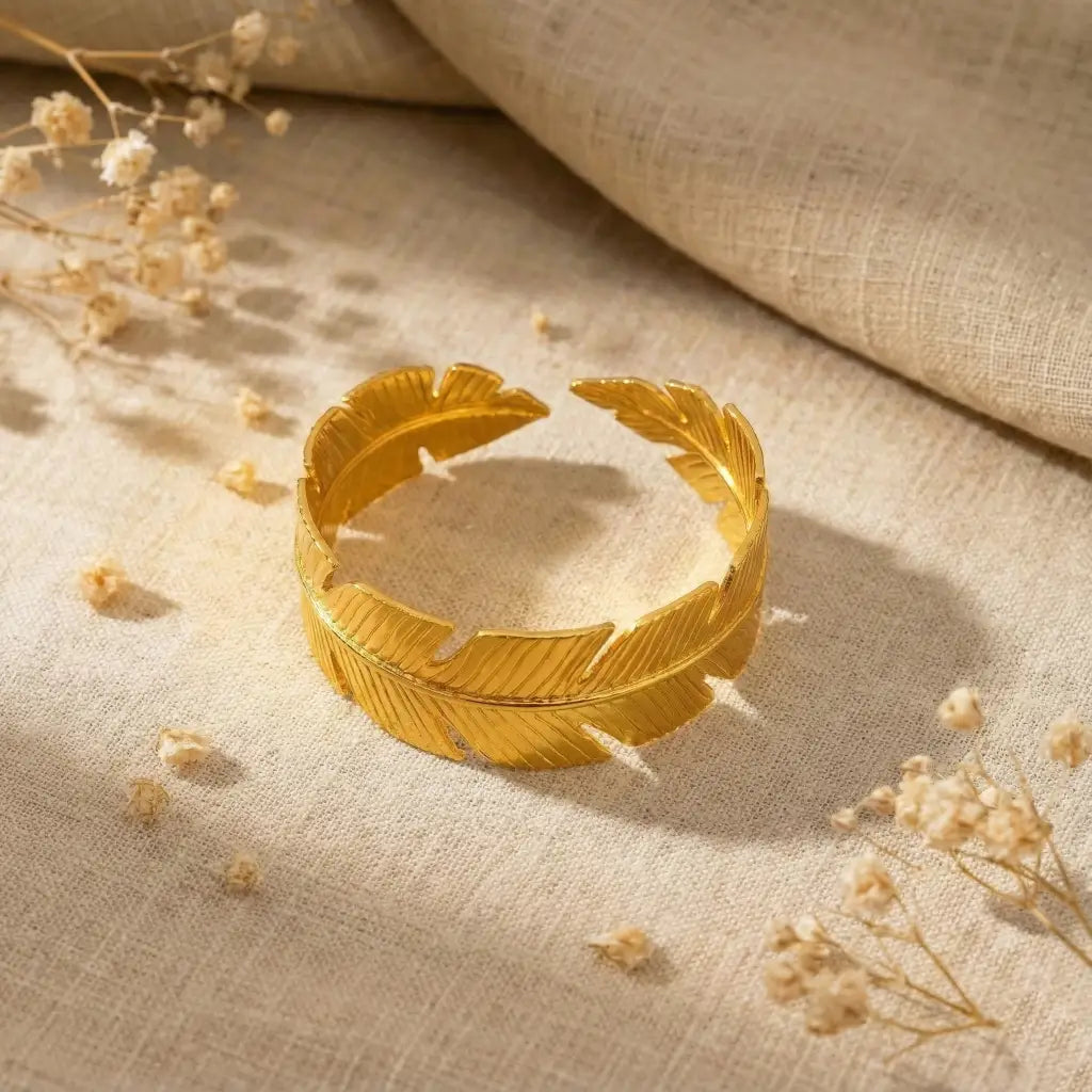 Gold leaf bracelet on a textured beige fabric background with dried flowers.