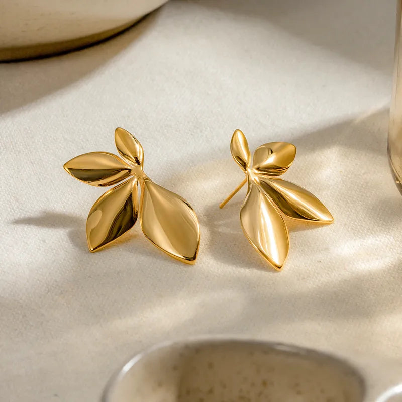 Gold leaf-shaped earrings on a beige surface