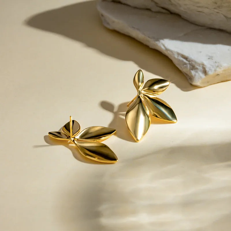 Gold leaf-shaped earrings on a beige surface with a stone background