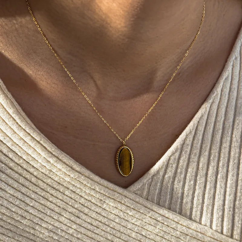 Gold necklace with a pendant worn by a person in a beige top.