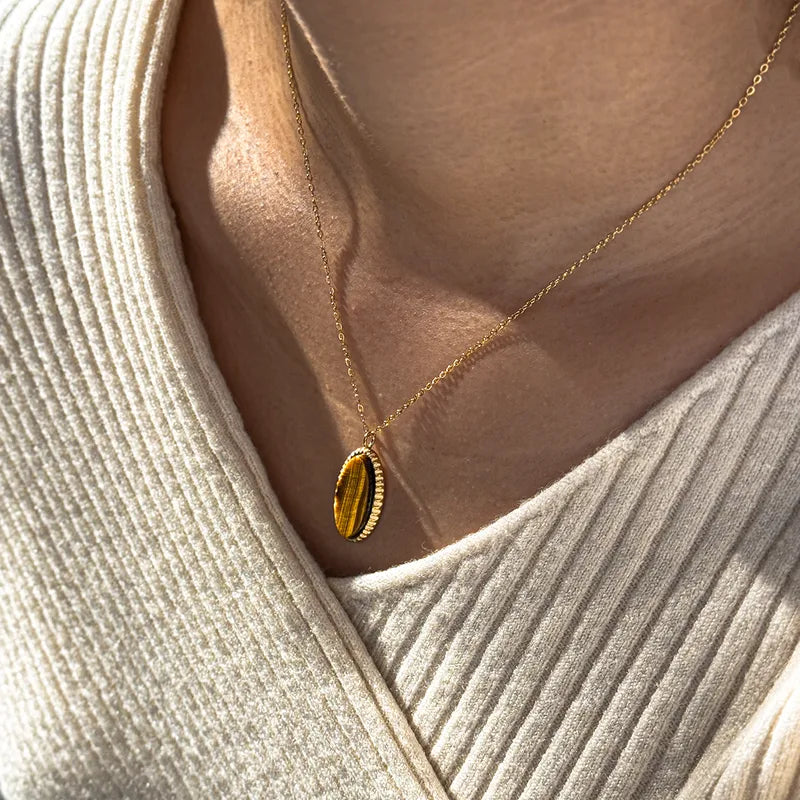 Gold necklace with a pendant worn by a person in a beige sweater.