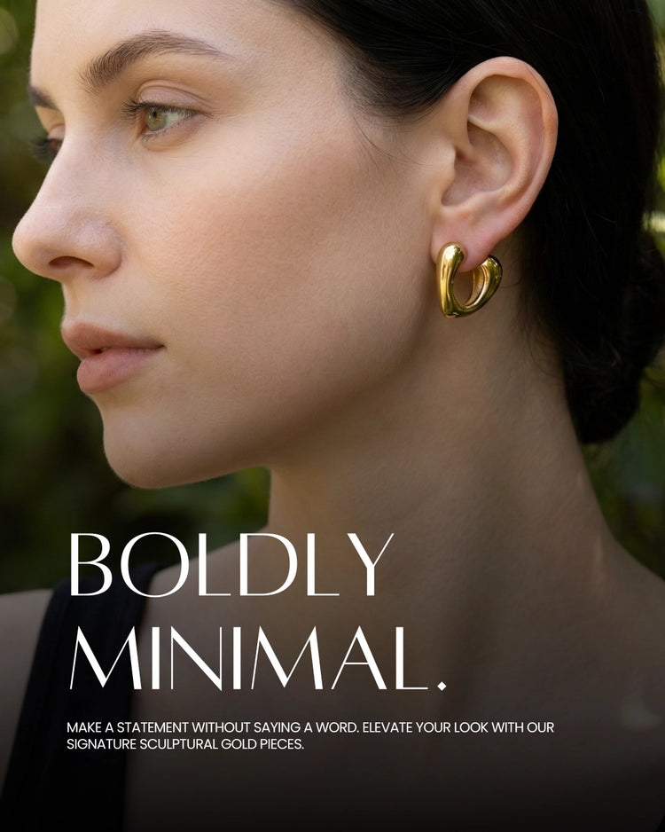 Close-up of a woman wearing gold hoop earrings with text 'BOLDLY MINIMAL' on a blurred natural background.