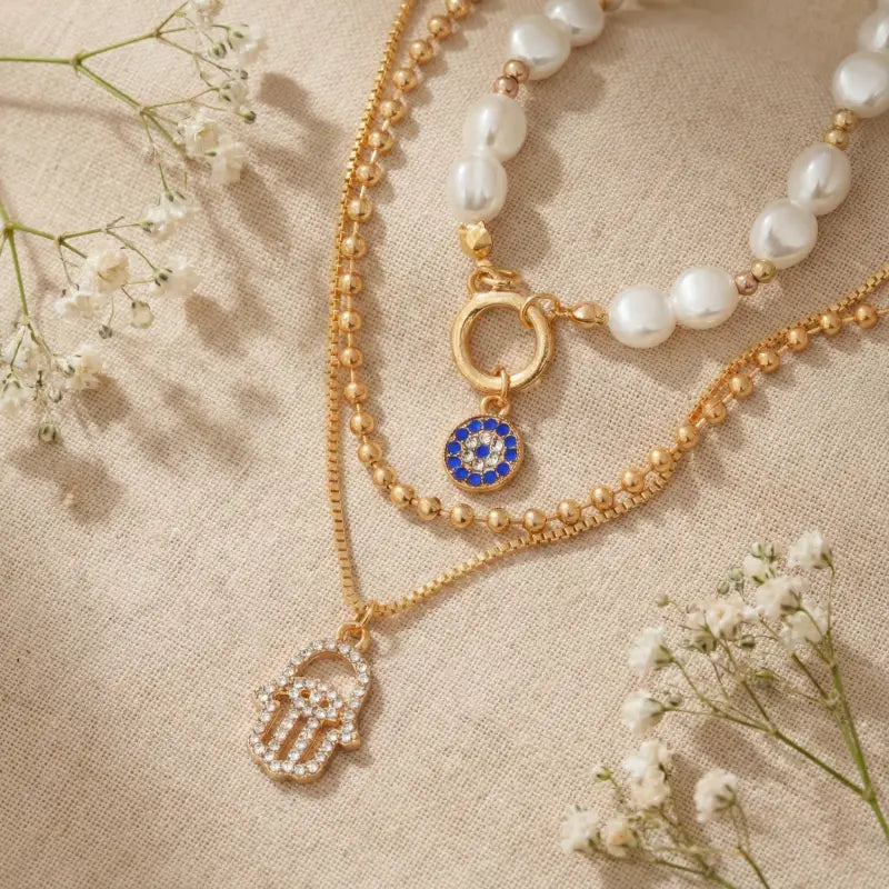 Two gold necklaces with charms on a beige fabric background with small white flowers.