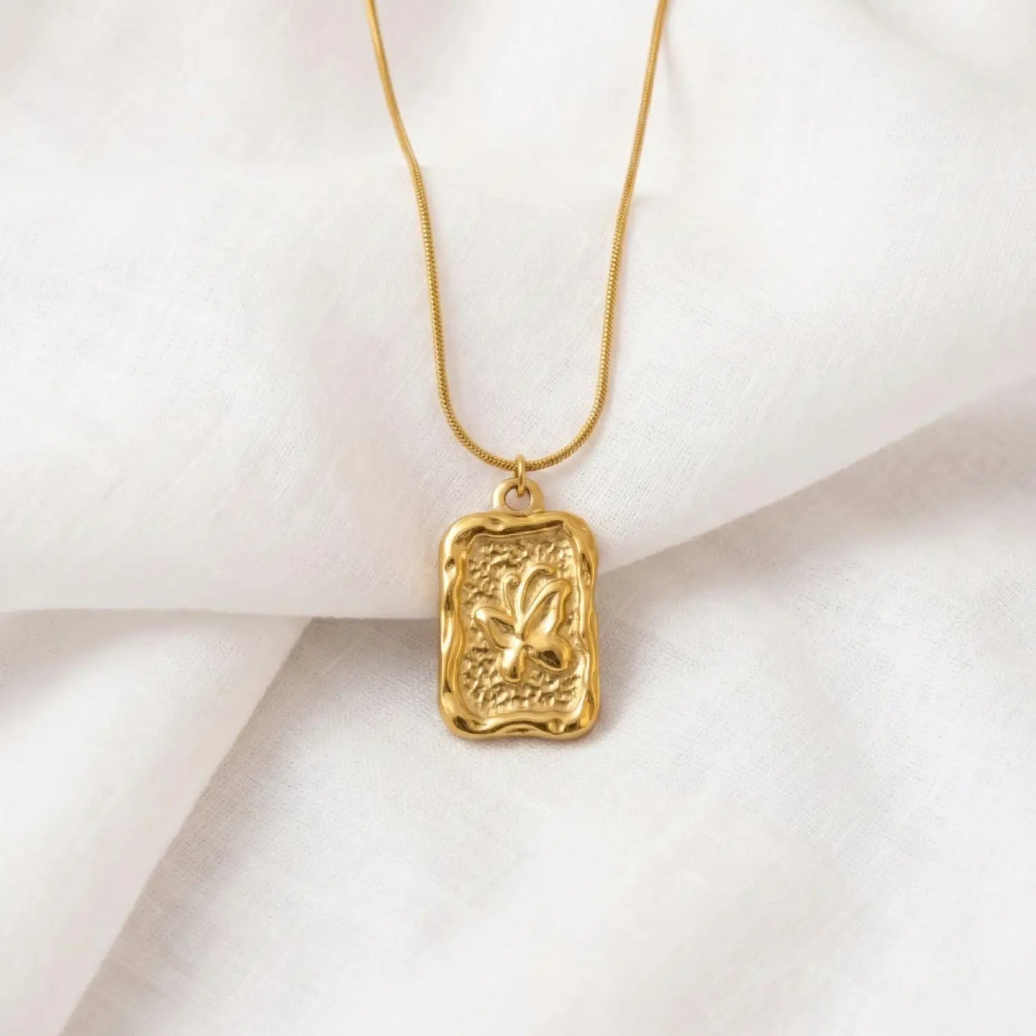 Gold necklace with a textured pendant on a white background