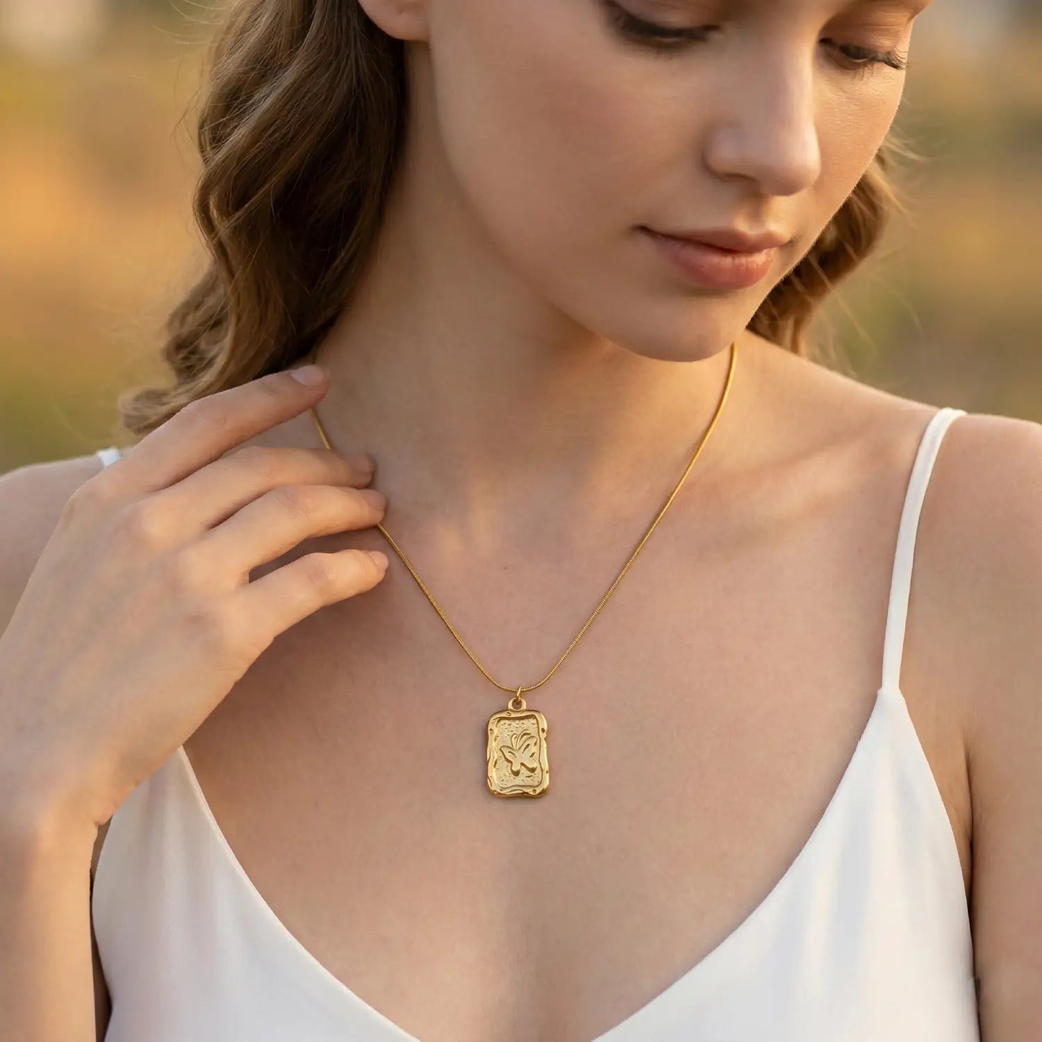 Woman wearing a gold necklace with a pendant in an outdoor setting