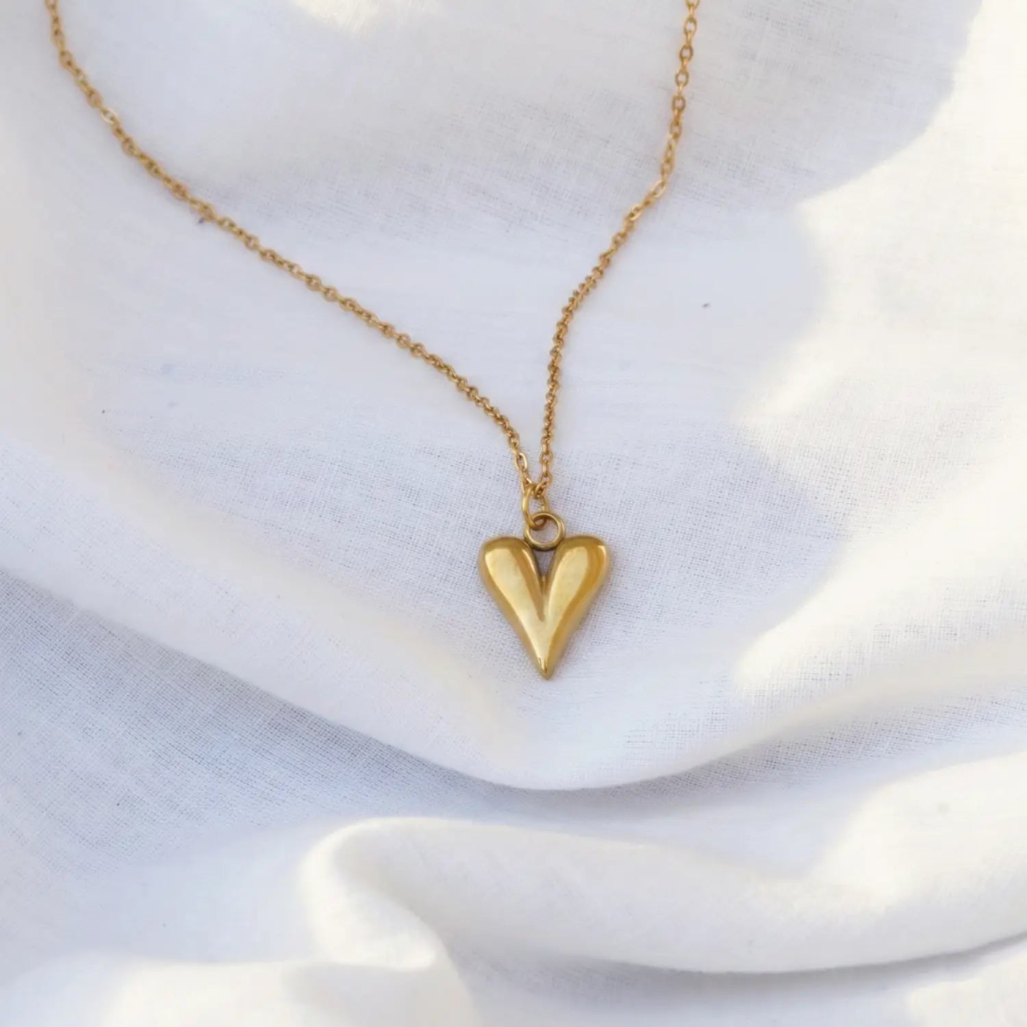 Gold heart-shaped pendant necklace on a white fabric background