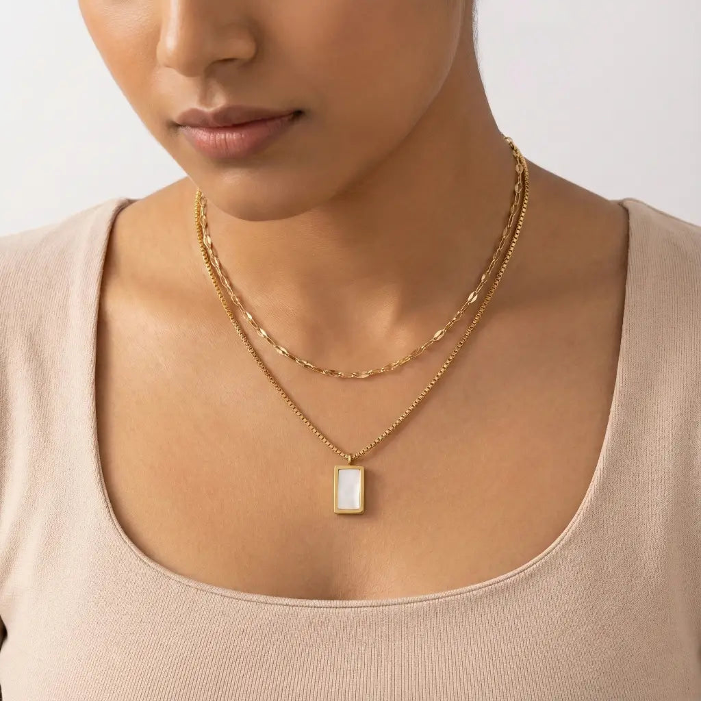 Woman wearing a gold necklace with a rectangular pendant on a neutral background