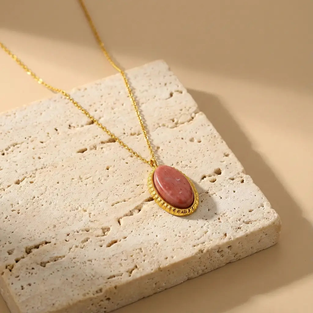 Gold necklace with a pink pendant on a textured stone surface