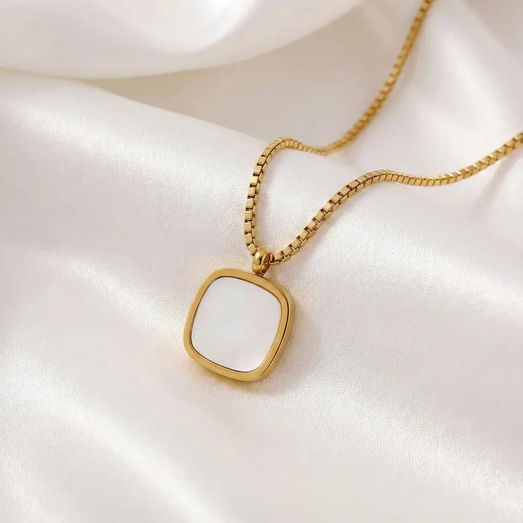Gold necklace with a white pendant on a white fabric background