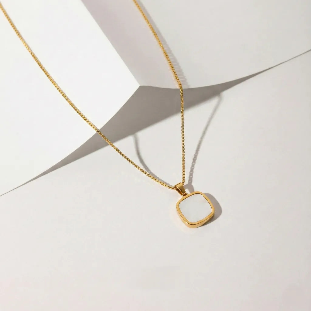 Gold necklace with a square pendant on a white background with  paper