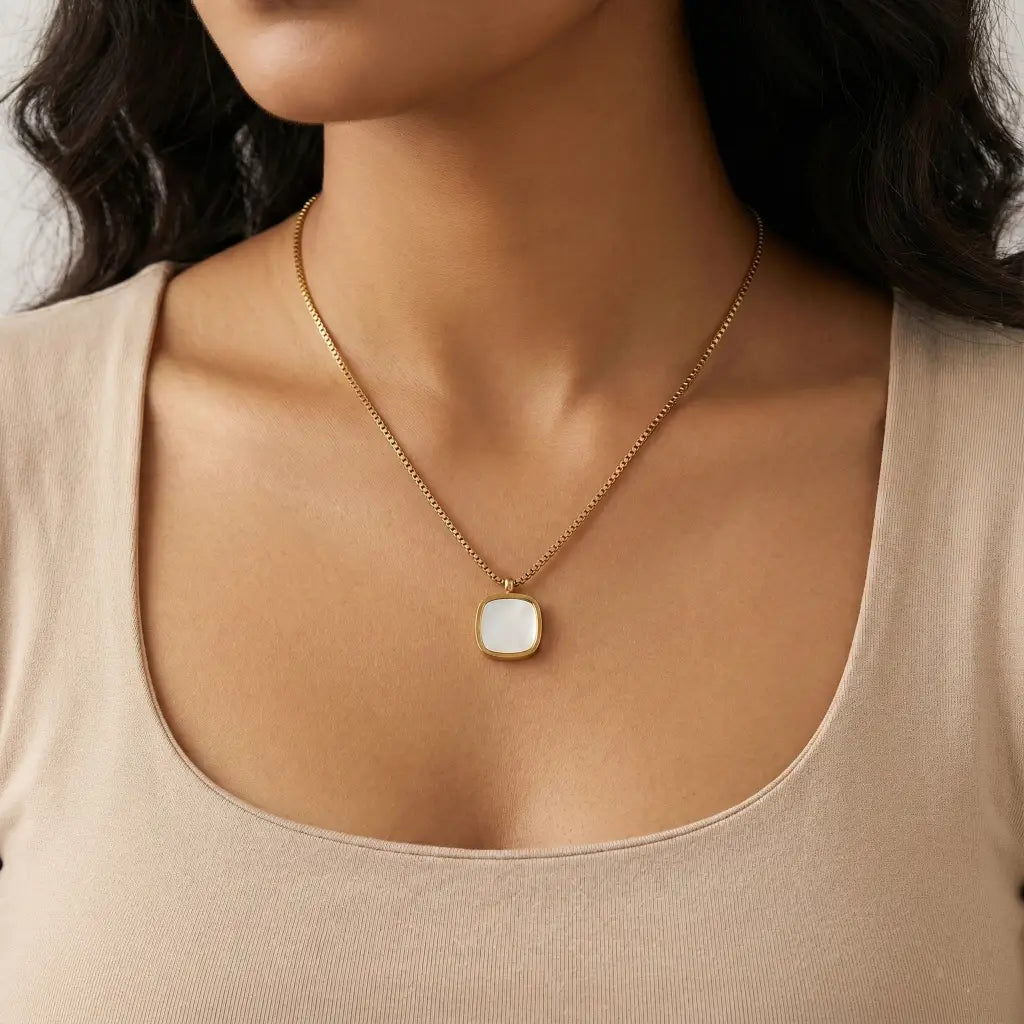 Necklace with a square pendant worn by a person in a beige top