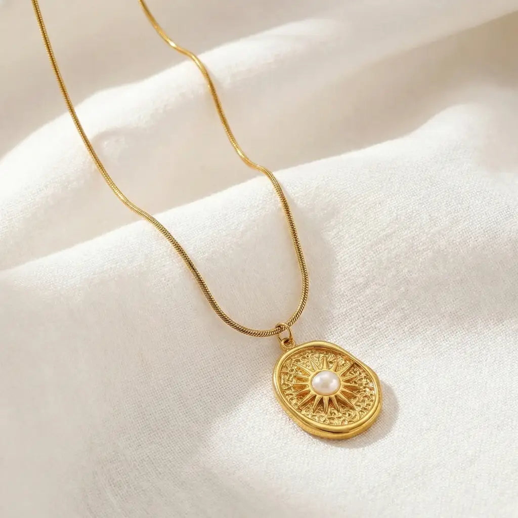 Gold necklace with a round pendant featuring a pearl on a beige surface